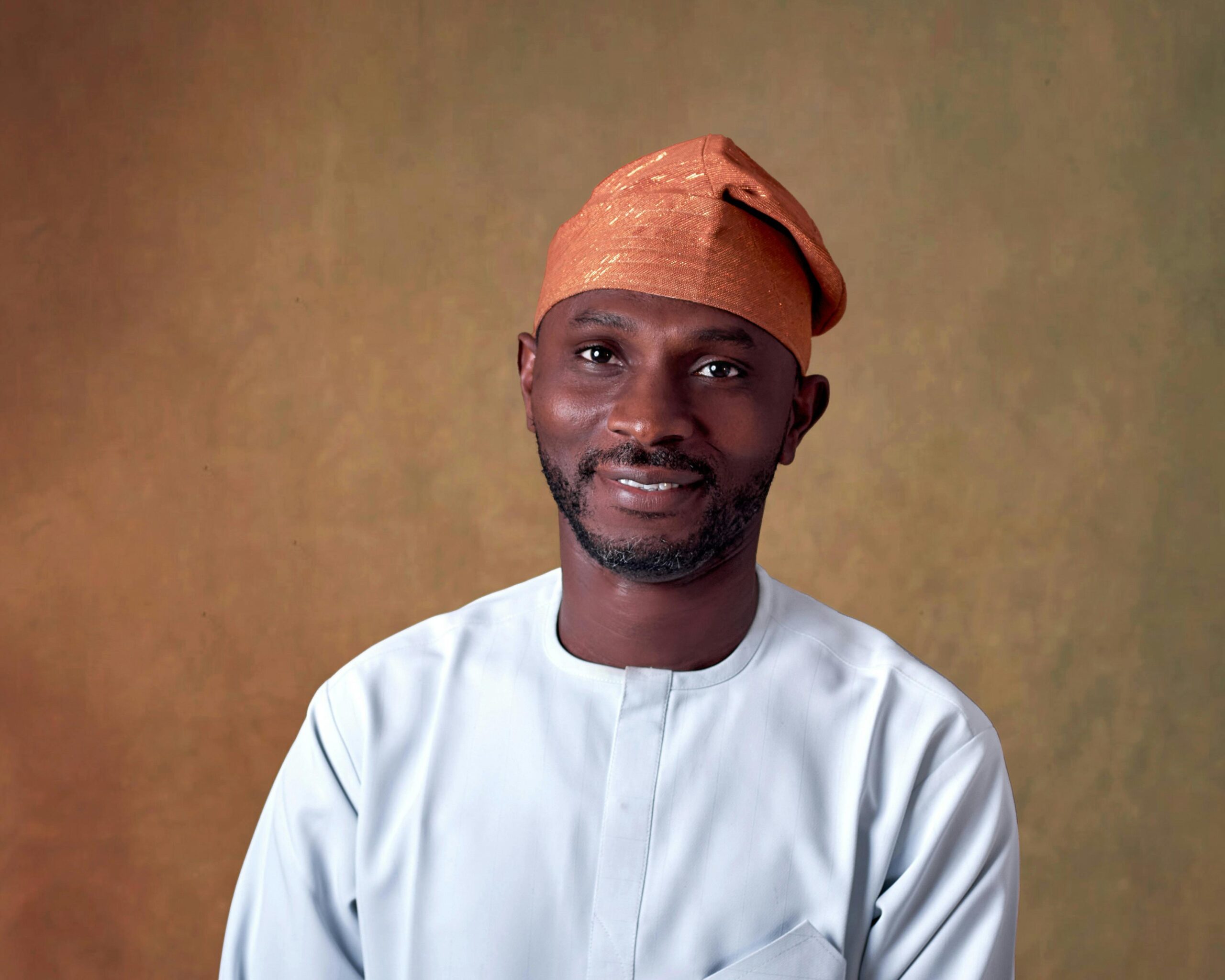 Smiling man in Nigerian attire and a cap with a warm, neutral background.